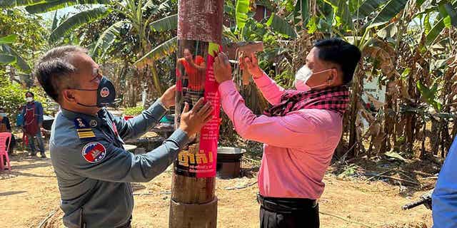 In this photo released by the Cambodia Ministry of Health, a Cambodia animal health officer, right, and a military police officer place posters about awareness of H5N1 virus threats in hopes of educating villagers to take care of their health in Prey Veng eastern province Cambodia, Feb. 23, 2023.