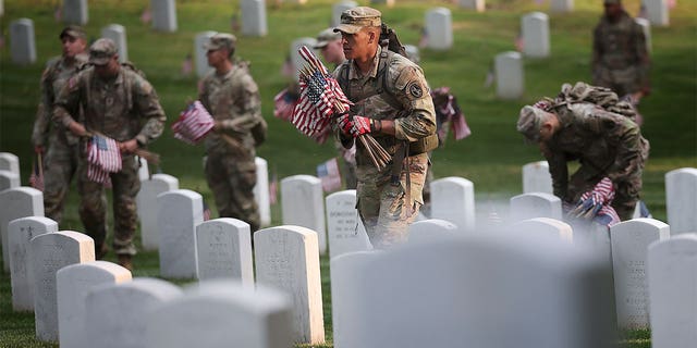 Military members placing flags on tombstones