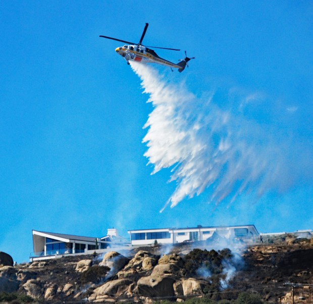 Firefighters drop water from a helicopter Sunday, Nov. 12, 2023, to protect a home from a 1-acre brush fire in Chatsworth. (Photo by Mike Meadows/Contributing photographer)