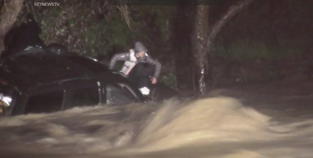 A person waits on top of his SUV in Cajon Creek in Devore on Feb. 5, 2024, after the vehicle got washed into the creek as a family of three tried to cross a flooded road. San Bernardino County firefighters were able to rescue them. (KEYNEWS.TV)